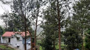 a white house with a red roof and some trees at jacaranda resorts in Kanthalloor