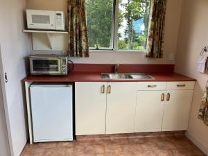 uma cozinha com armários brancos, um micro-ondas e um lavatório em Carrickfergus Cottage Unit 1 em Harihari