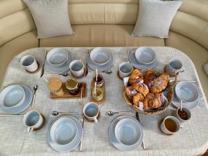 einen Tisch mit Tellern und Tassen sowie einen Korb mit Gebäck in der Unterkunft Jeanneau Sun Odyssey 54 DS LULU’ in Nydri