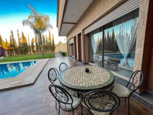 eine Terrasse mit einem Tisch, Stühlen und einem Pool in der Unterkunft agafay villa in Marrakesch