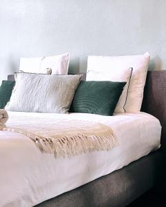 uma cama com lençóis brancos e almofadas verdes em Domus Portus em Dendermonde