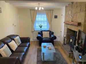 a living room with leather furniture and a fireplace at A Homely Welsh Cottage on Heol Maelor in Coedpoeth