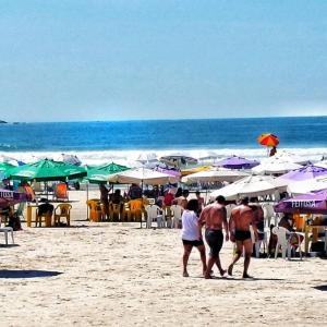 a group of people walking on a beach with umbrellas at Dom Pedro 55 in Guarujá