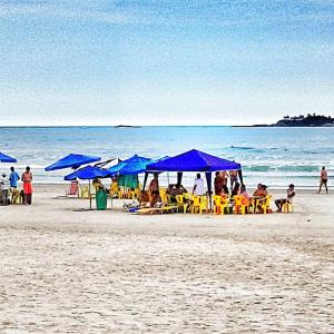 a group of people sitting under blue umbrellas on a beach at Dom Pedro 54 in Guarujá
