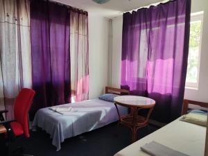 Zimmer mit 2 Betten, einem Tisch und lila Vorhängen in der Unterkunft Vila spatioasa 7 camere la lacul BUftea in Buftea