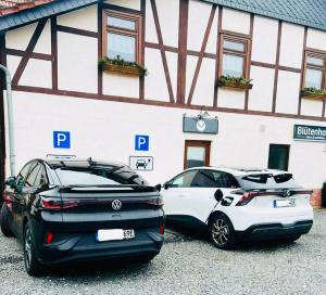 zwei Autos auf einem Parkplatz vor einem Gebäude geparkt in der Unterkunft Blütenhotel Village in Sarnau