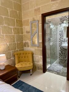 a bathroom with a yellow chair and a glass shower at Daner Ta’ Pantu House in Kerċem