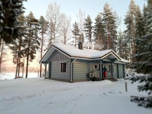 une personne debout à l'extérieur d'une petite maison dans la neige dans l'établissement Välituvan lomamökit, à Punkaharju