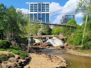 un puente sobre un río con una cascada y edificios en Cozy Swamp Rabbit - Sans Souci Greenville Furman en Greenville