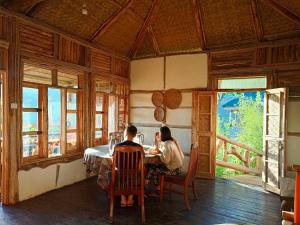 Dos personas sentadas en una mesa en una habitación con ventanas en Bwindi my home 