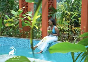 una mujer sentada en el borde de una piscina en Back to Roots Ayurveda Retreat, en Kizhake Chālakudi