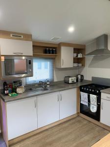 cocina con armarios blancos, fregadero y microondas en 4 Devon Country, Bideford Bay Holiday Park, en Bucks Mills