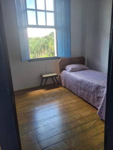 ein Schlafzimmer mit einem Bett, einem Fenster und einem Holzboden in der Unterkunft Fazenda centenária no Sul de MG 