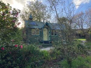 a green tiny house in a garden with roses at Enchanting Hand Painted Tabernacle with Hot Tub in Bude