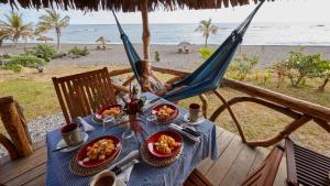 Eine Frau in einer Hängematte mit Essen auf einem Tisch am Strand in der Unterkunft Tanna friendly bungalow in Lénakel