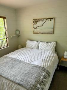 a bedroom with a white bed with a picture on the wall at The Bach at Te Toki in Palm Beach