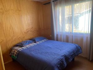 1 dormitorio con cama azul y ventana en Cabañas Rayen, en Riñinahue