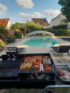 a grill with meat and other foods on it next to a swimming pool at VILLA avec piscine sauna barbecue ping-pong boxe - proche Gare RER - JO Paris 2024 Olympic Games in Combs-la-Ville