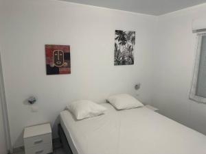 a white bed in a bedroom with two pictures on the wall at SLM - Le clos Gaïac - A in Saint-Laurent du Maroni