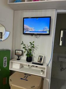 TV en la pared con escritorio y ordenador portátil en Quarto privativo em casa domiciliar en Campo Grande