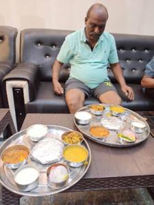 a man sitting on a couch with a tray of food at Guru Dev Palace Hotel & Lawn,Ayodhya in Ayodhya