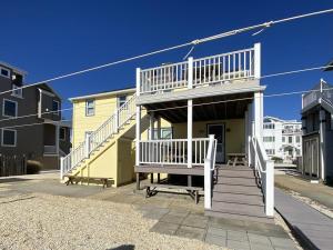 une maison jaune avec une terrasse blanche et des escaliers dans l'établissement Affordable Vacation Rental On Lbi, à Brighton Beach