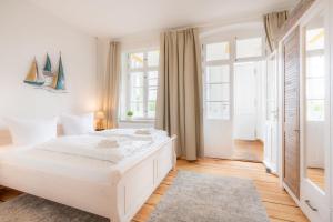 ein weißes Schlafzimmer mit einem großen weißen Bett und Fenstern in der Unterkunft Villa Albus App 2 in Ahlbeck