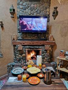 une table avec de la nourriture et une cheminée avec une télévision dans l'établissement Maison d'hôte tamatart - Homestay, à Kelaat-M'Gouna