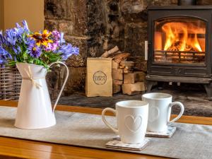 two coffee mugs and flowers in front of a fireplace at 2 Bed in Abergavenny 83894 in Llanover