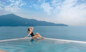 a woman sitting on a swimming pool in the water at A La Carte Da Nang Beach in Da Nang