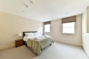a white bedroom with a bed and two windows at Sloane Square terraced house in London