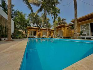 a swimming pool in front of a house with palm trees at The Nine Beach Resort in Canacona