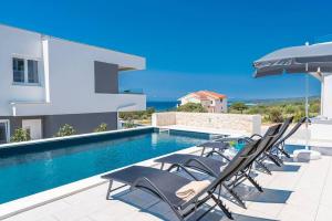 Cette villa dispose d'une piscine avec des chaises et un parasol. dans l'établissement Villa Adria 1, luxury apartment with a pool, à Novalja