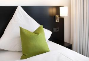 a white bed with a green pillow on it at NOM Hotel by WMM Hotels in Nörten-Hardenberg