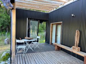 a black house with a table and a bench on a deck at Linda Cabaña pet friendly a orilla rio y bosque, cerca Termas in Panguipulli