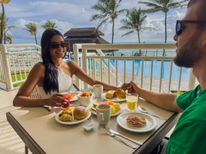 Um homem e uma mulher sentados à mesa a tomar o pequeno-almoço. em Aram Natal Mar Hotel em Natal