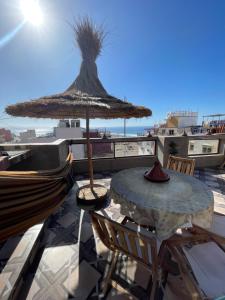 a table with a straw umbrella and chairs on a balcony at ASNFU AUBERGe in Imsouane