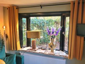 een raam met een vaas met bloemen en een lamp bij Verblijf midden in de natuur in de Jagershut! in Hattemerbroek