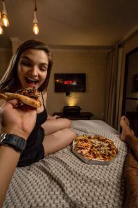 une femme assise sur un lit qui mange une tranche de pizza dans l'établissement Reserva do Paiva suites, à Cabo de Santo Agostinho