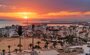 ALIYA LUXURY APARTMENT El HOUDA-AGADIR في أغادير: غروب الشمس على مدينة بها شاطئ ومباني