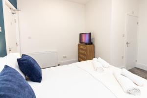 Suite 1 - Lovely Ensuite in Oldham Sociable House في أولدهام: غرفة نوم مع سرير أبيض مع وسائد زرقاء وتلفزيون