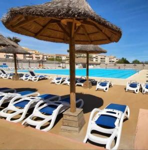 a group of lounge chairs and an umbrella at a pool at Bungalow dans une résidence en plein air a l'Elysée vagues océanes "capfun" in Le Grau-du-Roi