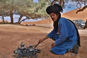 a man is lighting a tea pot over a fire at Golden Camp & Oasis in Merzouga