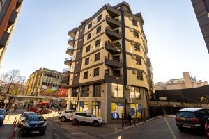 a tall building with cars parked in a parking lot at Harizma apartmani - Iris in Kragujevac