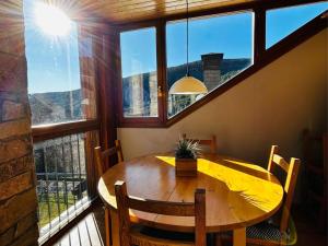 una mesa y sillas en una habitación con ventanas grandes en Casa Mya. A Modern Duplex in the Spanish Pyrenees, en Aso de Sobremonte