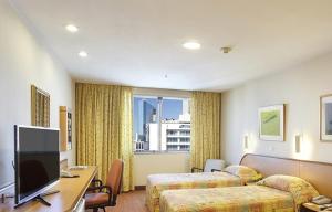 um quarto de hotel com duas camas e uma secretária com uma televisão em Windsor Guanabara Hotel no Rio de Janeiro