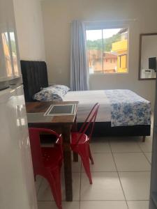 1 dormitorio con 1 cama y 1 mesa con sillas rojas en Comodidade e simplicidades a 240m do mar, en Florianópolis