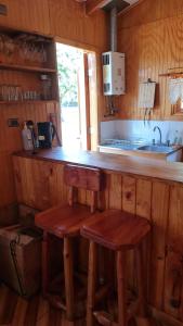 een keuken met een bar en 2 krukken bij Cabañas Canto del Tiuque in Pishuinco