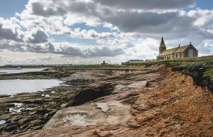 a church on a hill next to a body of water at Château by the Sea - Luxury hotel style 3 bed with hot tub in Newbiggin-by-the-Sea