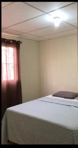 a bedroom with a bed with a white blanket and a window at Kami Hostel, Ciudad El Doral in Managua